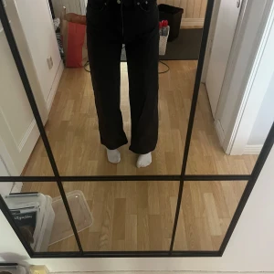Svarta vida jeansbyxor - Säljer ett par svarta jeansbyxor med hög midja och raka, vida ben. Klassisk femficksmodell med knapp och dragkedja framtill. Perfekta för en avslappnad och trendig look.
