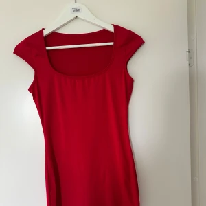 Röd tight klänning med bred ringning - En enkel och stilren röd klänning med bred, fyrkantig ringning och korta ärmar. Modellen är tight och passar perfekt för dig som gillar en minimalistisk look. Klänningen är tillverkad i ett mjukt och stretchigt material.
