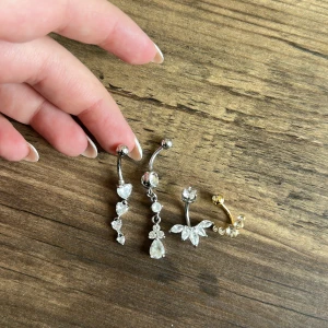 Navelpiercingar  - Tre navelpiercingar i silver med glittrande stenar och en i guldfärg med blommig design. Alla gjorda av kiruriskt stål. Aldrig använda💕