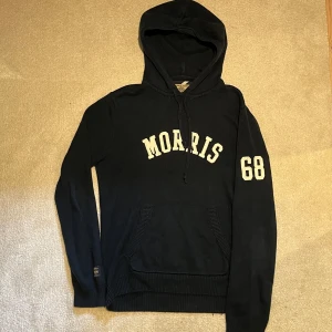 Stickad Morris hoodie  - Tja! Säljer en mörkblå hoodie från Morris med vit text på bröstet och siffran 68 på ärmen. Tröjan har huva med dragsko och en stor magficka framtill. Perfekt för kyliga sommarkvällar. Vid minsta fråga eller fundering hör av er🤝