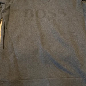Mörkgrå sweatshirt från Hugo Boss - Säljer en mörkgrå sweatshirt från Hugo Boss med diskret BOSS-logga framtill. Tröjan har lång ärm och är i slim fit-modell, perfekt för en stilren och enkel look.