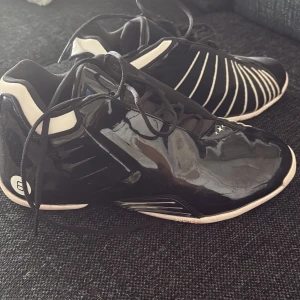 Basket skor  - Säljer ett par svarta basketskor från Adidas med blanka partier och vita ränder på sidorna. Skorna hata när använts några gånger annars ser de nya ut. 
