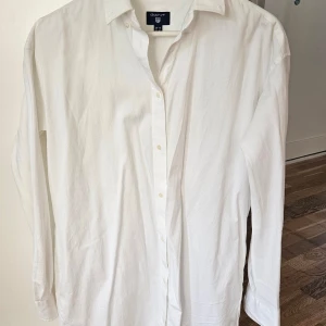 Vit skjortklänning från Gant 38 - Klassisk vit skjortklänning från Gant med krage och knäppning framtill. Skjortklänningen har lång ärm och fickor och är tillverkad i 100% bomull, perfekt för en stilren look. 