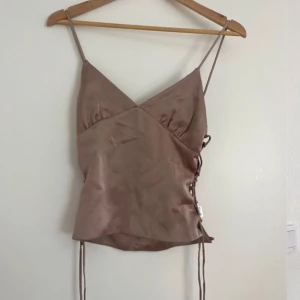 Brun satin topp  - Snygg brun satin topp med smala axelband och knytning i sidan. 