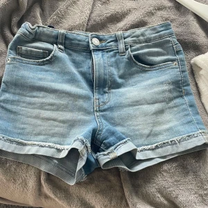 Ljusblå jeansshorts från LAB Industries - Säljer ett par ljusblå jeansshorts från LAB Industries med fransade benslut och klassisk femficksdesign. Shortsen har knapp och dragkedja framtill samt bälteshällor. Perfekta för varma dagar!