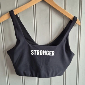 Svart sport-bh från Stronger M - Svart sport-bh storlek M från Stronger med breda axelband och vit logotyp framtill. Perfekt för träning och ger bra stöd. Enkel och stilren design som passar till det mesta i träningsgarderoben.