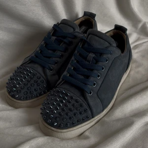 Christian loubition( Washed blue ) - Säljer ett par sneakers från Christian Louboutin med coola nitar på tån och klassisk röd sula. Skorna har blå snörning och är tillverkade i mocka med vit platt sula. Perfekta för dig som vill sticka ut med din stil.