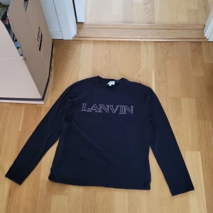 Svart långärmad tröja från Lanvin - Säljer en svart långärmad tröja från Lanvin med tryckt logga över bröstet. Tröjan har en klassisk passform och rund halsringning. Perfekt för dig som gillar stilrena och exklusiva plagg.
