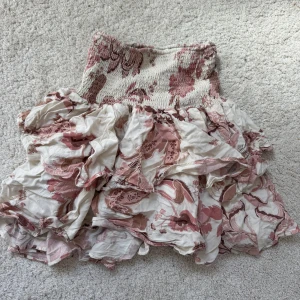 Rosa och vit volangkjol från Sofie Schnoor - Supersöt kortkjol från Sofie Schnoor i rosa och vitt med blommigt mönster och volanger. Kjolen har smock i midjan för en bekväm passform och är perfekt för vår och sommar.