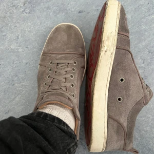 Loubs utan spikar   - Säljer ett par beige sneakers i mocka med snörning och rund tå. Skorna har en vit platt sula och diskret design, perfekta för en avslappnad stil. Passar till många olika outfits och är riktigt bekväma.