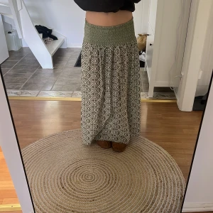 Grönmönstrad långkjol med smock - Säljer en långkjol med bred smock i midjan och grönt, vitt mönster. Kjolen är luftig. Perfekt för varma dagar, kjolen är storlek L men passar även M och S