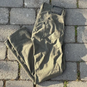 Olivgröna jeansbyxor från Levi's 513 - Säljer ett par olivgröna Levi's 513 jeans med klassisk femficksdesign och raka ben. Byxorna har en svart patch bak i midjan och Levi's signaturmärke vid bakfickan. Perfekta för dig som gillar tidlös stil och vill ha ett par jeans som funkar till det mesta.