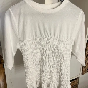 Vit topp med smock och volang - Säljer denna trendiga t shirt från hm, nästan i helt nytt skick utan defekter.