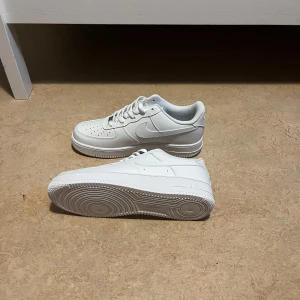 Vita Nike Air Force 1 sneakers - Säljer ett par klassiska vita Nike Air Force 1 sneakers. Skorna har en stilren design med perforerad tå, snörning och låg profil. Perfekta för dig som vill ha en clean och tidlös look. Passar till det mesta och är riktigt bekväma.