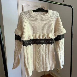Vit stickad tröja med spetsdetalj från Zara - Säljer en vit stickad tröja från Zara med kabelstickat mönster och volangdetalj. Tröjan har en svart spetsdetalj över bröstet och långa ärmar. Perfekt för dig som gillar unika detaljer och eleganta plagg.