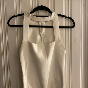 Vit ärmlös linnetopp med hög hals - Snygg vit linnetopp med hög hals och breda axelband. Toppen har en stilren, minimalistisk design med rak passform och dragkedja i ryggen. Perfekt för dig som gillar en clean och modern look.