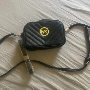 Svart axelväska Michael Kors - Snygg svart axelväska från Michael Kors med guldiga detaljer och MK-logga framtill. Väskan är quiltad i ett chevronmönster och har justerbar axelrem samt dragkedja upptill. Perfekt storlek för det viktigaste och stilren design som lyfter varje outfit. Nyskick❤️