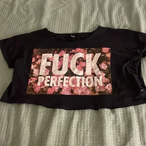 Svart croppad topp 77th Flea - Svart croppad topp från 77th Flea med stort tryck framtill. T-shirten har korta ärmar och en loose passform. 