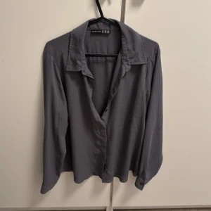 Grå skjorta från Atmosphere - Stilren grå skjorta från Atmosphere i storlek 40. Skjortan har klassisk krage, långa ärmar med knapp vid ärmslut och en rak passform. Perfekt att styla med jeans eller kjol för en clean look.