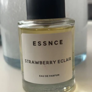 ESSNCE Strawberry Eclair parfym - En söt och fruktig eau de parfum från ESSNCE med doft av jordgubb och bakverk. Kommer i en genomskinlig glasflaska med svart lock och stilren vit etikett. Perfekt för dig som gillar gourmanddofter med en lekfull twist.