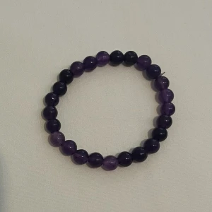 Lila pärlarmband med stenar - Snyggt armband med runda, glansiga pärlor i olika nyanser av lila. Pärlorna är trädda på en elastisk tråd vilket gör det enkelt att ta på och av. Perfekt accessoar för att ge din outfit lite extra färg och stil.