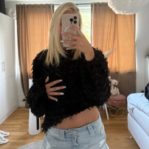 Svart fluffig stickad tröja - Säljer en svart fluffig stickad tröja med lång ärm och rund hals. Tröjan har en cool, lite oversized passform och är supermjuk med en unik textur som ger en trendig look. Perfekt att styla med jeans eller kjol för en chill vibe.