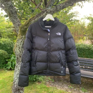 Svart dunjacka från The North Face - Säljer en svart dunjacka från The North Face i storlek XS. Jackan har en klassisk pufferstil med hög krage, dragkedja framtill och två fickor med dragkedja. Perfekt för kalla dagar och riktigt skön att bära. Logga på bröstet och ryggen. Nypris ca 3000, mitt pris 2000