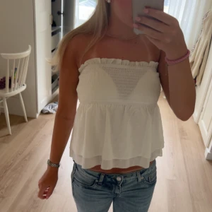 Vit bandeau tubtopp med volang - Supersöt vit bandeau tubtopp. Toppen är ärmlös och har ett luftigt, dubbellager tyg. 
