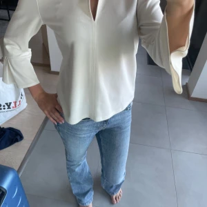 Vit blus med trumpetärm från H&M - Säljer en stilren vit blus från H&M i storlek XS. Blusen har trekvartsärmar med trumpetformad avslutning och en snygg v-ringning framtill. Materialet är mjukt och har ett lätt fall, perfekt för en clean och fräsch look.