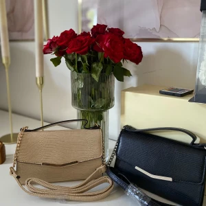 2 st eleganta handväskor  - Två stilrena axelväskor, en i beige och en i svart. Väskorna har kedjedetaljer, smidig magnetknäppning och ett elegant handtag upptill. Perfekt storlek för det viktigaste och snygg detalj till din outfit.