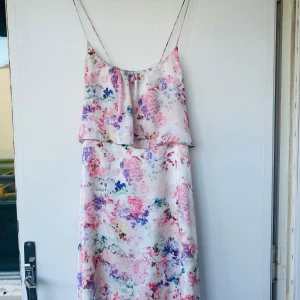 Blommig klänning från Gina Tricot - Superfin sommarklänning med tunna axelband från Gina Tricot. Klänningen har ett romantiskt blommigt mönster i rosa, lila och blå toner på vit botten. Sval och flowy modell i glansigt material, perfekt för sommarens alla tillfällen.