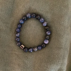 Blått pärlarmband med metallpärla - Snyggt armband med blå marmorerade pärlor och en cool silverfärgad metallpärla som detalj. Elastiskt band gör det enkelt att ta på och av. Perfekt accessoar för att lyfta din outfit med lite extra stil.