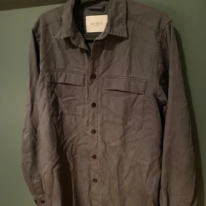Grå overshirt från Les Deux - Snygg grå overshirt från Les Deux med klassisk krage, två bröstfickor med lock och knäppning framtill. Skjortan är tillverkad i bomull och har långa ärmar med knapp vid ärmslut. Perfekt lager-på-lager-plagg för en clean look.