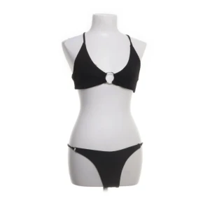Svart bikini med ringdetalj - Stilren svart bikini med smala axelband som korsas i ryggen och en snygg ringdetalj framtill. Var lite för liten i bysten (har C kupa). Perfekt för strandhäng och poolparty!