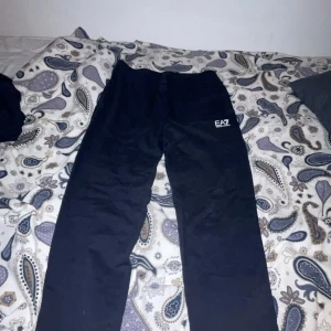 Svarta mjukisbyxor från EA7 Emporio Armani - Svarta mjukisbyxor från EA7 Emporio Armani med logga på vänster lår och diskret detalj på baksidan. Byxorna har en avslappnad passform och är perfekta för chill eller träning. Använd endast ett fåtal gånger. Storlek S. 