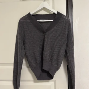 Mörkgrå kofta från NA-KD med v-ringning - Säljer en mörkgrå kofta från NA-KD i storlek XS. Tröjan har v-ringad hals, lång ärm och ett snyggt fiskbensmönster i tyget. Ribbstickade muddar vid ärmslut och nederkant ger en schysst passform. Perfekt till lager-på-lager-stil.