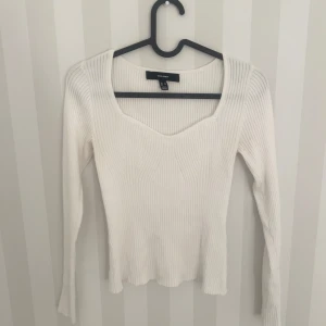 Vit ribbad tröja från Vero Moda - Supersnygg vit ribbad tröja från Vero Moda med lång ärm och en unik v-ringad halsringning. Tröjan är figurnära och har en stretchig, stickad känsla som gör den både bekväm och stilren. Perfekt att matcha med jeans eller kjol för en clean look.