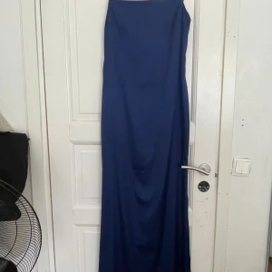 Marinblå långklänning från Nelly - Säljer en elegant marinblå långklänning från Nelly i storlek 36. Klänningen har axelbandslös design och är figurnära med en stilren siluett. Materialet är glansigt och känns lyxigt, perfekt för speciella tillfällen. Dragkedja i ryggen för enkel påklädning.