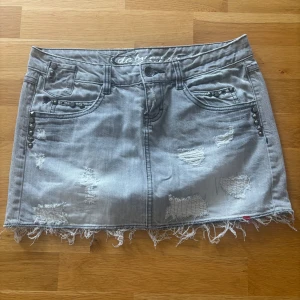 Grå jeanskjol med nitar från Esprit - Snygg grå jeanskjol från Esprit med slitna detaljer, fransig nederkant och coola nitar på fickorna. 