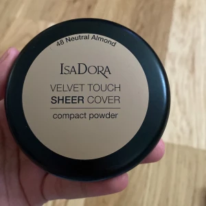IsaDora Velvet Touch Sheer Cover puder - IsaDora Velvet Touch Sheer Cover compact powder i nyansen 48 Neutral Almond. Pressat puder i en rund svart dosa med spegel, ger en naturlig och lätt täckning. Perfekt för att matta ner huden och jämna ut hudtonen. Färgen är en neutral beige med varm underton. Ligger i Vetlanda.helt nytt har aldrig använt.