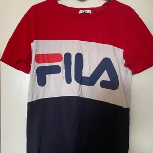 FILA t-shirt - Snygg t-shirt från FILA med stora loggan framtill. Tröjan har blockfärger i rött, vitt och mörkblått, klassisk rund hals och korta ärmar. Tillverkad i mjuk bomull som är skön mot huden. Perfekt för en sportig och avslappnad look. Frakt tillkommer