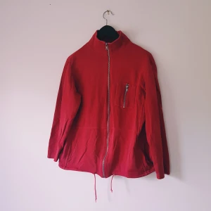 Röd ribbad ziptröja från veromoda strl M - Röd ribbad ziptröja med hög krage, hel dragkedja framtill och snörning i nederkant. Tröjan har en bröstficka med dragkedja och är långärmad. Perfekt för dig som gillar enkel och sportig stil.  Början till hål, noppror & ljusare i färgen