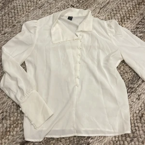 Vit blus - Snygg vit blus från SHEIN i storlek M med lång ärm, stora manschetter och dekorativa knappar framtill. 