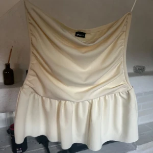 Krämvit bandeau topp från Gina Tricot - Supersöt krämvit bandeau topp från Gina Tricot med volang nedtill. 