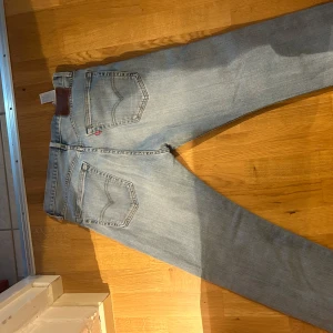 Levi's 501 ljusblå jeans straight fit - Klassiska Levi's 501 jeans i ljusblå tvätt med raka ben och knappgylf. Jeansen har fem fickor, ikonisk röd Levi's-tag och läderpatch bak i midjan. Perfekta för en avslappnad och tidlös stil.