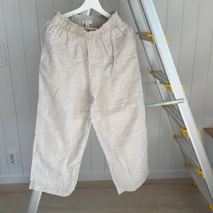 Beiga linnebyxor från H&M, storlek S - Säljer ett par ljusbeiga linnebyxor från H&M i storlek S. Byxorna har resår i midjan för extra komfort och en avslappnad, loose passform. Perfekta för varma dagar när du vill ha något svalt och stilrent.