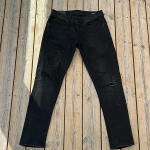 Dondup George  - Svarta jeans från dondup med coola slitningar och vita färgstänk på både fram- och baksida. Klassisk femficksmodell med smal passform och diskret broderad detalj på bakfickan. Perfekta för en edgy streetstil.