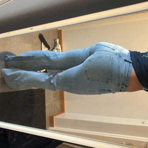 Ljusblå bootcut jeans från H&M - Säljer ett par ljusblå H&M jeans med bootcut passform och klassisk femficksdesign. Jeansen har hög midja och raka ben som blir vidare nertill. Tillverkade i mjukt denimtyg med bälteshällor och dragkedjegylf. Perfekta för en chill och trendig look.