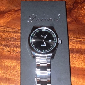 Klocka(HELT NY) - En riktigt fet klocka köpte en klocka fick hem den idag men den var lite stor och satt lite konstigt så derför säljer jag den här på plick den har en mörk blå urtavla med snygg decine jätte bra för dig om du behöver en ny klocka som du kan ha i skolan eller bara ha på vardagen skriv till mig vid några funderingar pris kan diskuteras så skriv till mig om du är intresserad så kan vi diskutera pris.