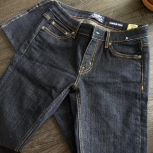 Crocker mörkblå bootcut jeans - Snygga mörkblå jeans från Crocker med klassisk femficksdesign och kontrastsömmar. Modellen är bootcut med normal passform och tillverkad i slitstarkt jeanstyg. Perfekta för dig som gillar en tidlös look med lite utsvängda ben.